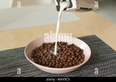 Schokolade Müsli Kugeln mit Milch in einer Schale auf der Serviette auf Holztisch. Trockene Frühstücksflocken Kugeln. Gesundes Frühstück Konzept. Stockfoto