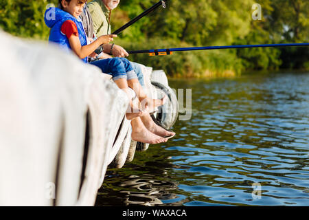 Junge sitzt in der Nähe von Vater und Großvater in Jeans hochgezogen, während die Fischerei