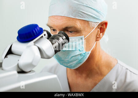 Schwere reifen Arzt sitzen vor dem Mikroskop Stockfoto