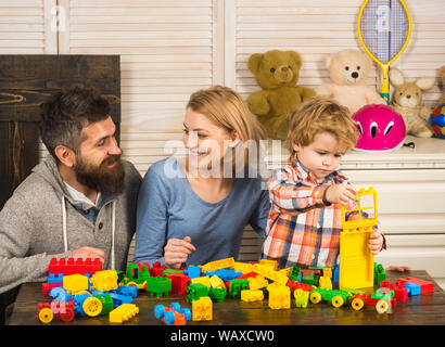 Eltern mit glücklichen Gesichtern und Kid macht brick Konstruktionen. Vater, Mutter und Sohn im Spielzimmer auf hellen Hintergrund. Familie Zeit Konzept. Junge Stockfoto