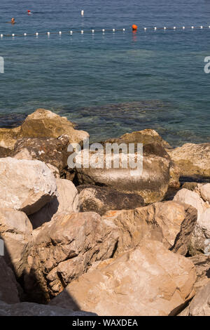 Große Steine Futter das Wasser der Adria. Klares ruhiges Wasser. Leitung der Bojen markiert den Strand. Primosten, Kroatien. Stockfoto