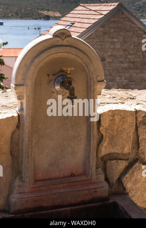 Waschbecken aus Stein, mit einem Bogen. In einem Park von einem St. George Kirche entfernt. Haus und Meer im Hintergrund. Primosten, Kroatien. Stockfoto