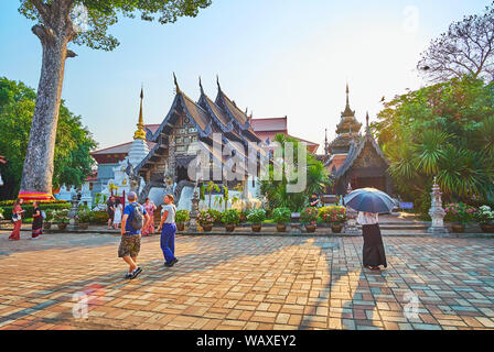 CHIANG MAI, THAILAND - Mai 2, 2019: Der üppige Garten mit dipterocarp Tree, Palmen und Blumen in Töpfe vor der alten Teak Tempel von Wat Chedi Lua Stockfoto