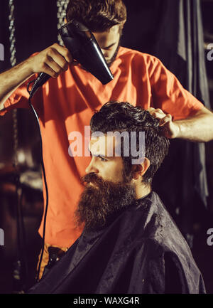 Stattliche Friseur Haar Trocknen, Trockner, macht Frisur, bärtiger Mann mit Bart. Männliche Kunden im Stuhl sitzen im Friseursalon oder barbersho Stockfoto