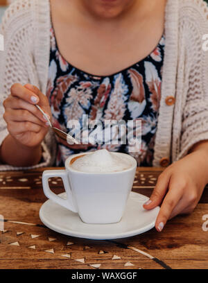 Asiatische Frau mit Löffel über Cappuccino Kaffee in weißen Schale auf alten Holztisch, schoß schließen. Stockfoto