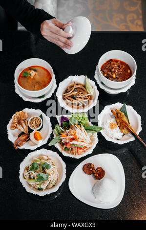 Verschiedene traditionelle Thai Essen, rot Massaman Curry, Tom Yum würzige Suppe, Papaya Salat, gegrilltes Hühnchen und lokale Gerichte auf schwarz Table Top view Shot Stockfoto