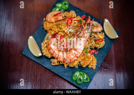 King Prawn Paella spanische Paella Reis mit roten und grünen Pfeffer Chili auf schwarzen Stein auf Holz Tisch Stockfoto