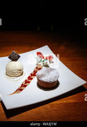 Französische Dessert. Schokolade Fondant lava Kuchen mit Vanilleeis, cremige Soße und frische Erdbeeren mit Schlagsahne. Weiß Nachtisch auf Holz Stockfoto