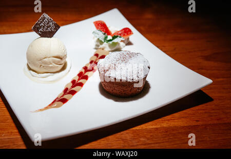 Französische Dessert. Schokolade Fondant lava Kuchen mit Vanilleeis, cremige Soße und frische Erdbeeren mit Schlagsahne. Weiß Nachtisch auf Holz Stockfoto
