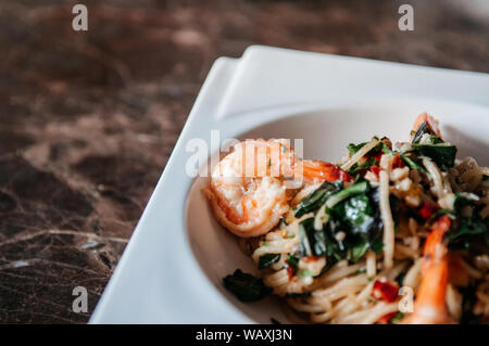 Fusion Pasta spicy thai Pad Kapraw Spaghetti mit Knoblauch, Chilischote, Garnelen und Heiliges Basilikum in Weiß Platte auf dem Marmortisch. Stockfoto