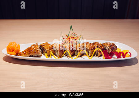 Schöne Stücke der Japanischen gegrillte Unagi Maki Rollen auf weiße Platte mit dunklem Hintergrund Stockfoto