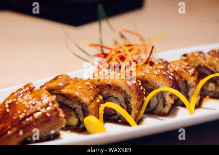 Schöne Stücke der Japanischen gegrillte Unagi Maki Rollen auf weiße Platte mit dunklem Hintergrund Stockfoto