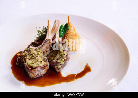 Kellner serviert gegrillte Lammkoteletts mit Kruste, Soße und frittierte Kartoffeln, aus nächster Nähe erschossen Stockfoto
