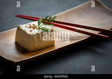 Block von Tofu in Nahaufnahme auf Holzplatte und Essstäbchen Stockfoto
