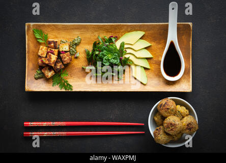 Platte mit Tofu, Gemüse und Avocado auf schwarzer Stein mit falafel und Chinesische essstäbchen eingerichtet Stockfoto