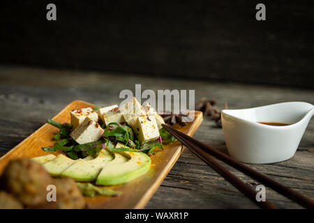 Tofu in Nahaufnahme mit Stäbchen, Gemüse, Obst und Gewürze und Schüssel von Sojasoße Stockfoto