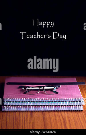 Happy Teachers' Day auf einer Tafel mit einem von Büchern oder Zuordnungen, Gläser, Stifte und Lineal auf einen hölzernen Tisch Stapel geschrieben. Kopieren Sie Platz. Stockfoto