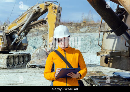 Weibliche Geologe oder ein bergbauingenieur Schreibt etwas in einer Karte - Fall mitten in einem Steinbruch mit Baumaschinen Stockfoto