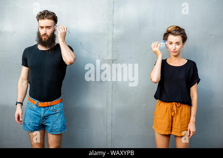 Mann und Frau im Gespräch mit Zeichenkette Telefon von Cups auf dem grauen Hintergrund. Konzept der Kommunikation Stockfoto