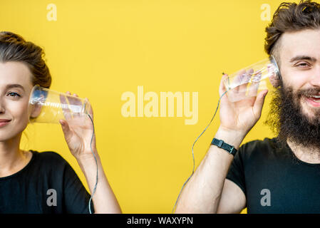 Mann und Frau im Gespräch mit Zeichenkette Telefon von cups auf den gelben Hintergrund. Konzept der Kommunikation Stockfoto