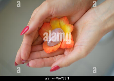 Weibliche hand mit roten Maniküre Holding transparent violett Amethyst yoni Ei für vumfit, imbuilding oder Meditation in Orange und Gelb gladiolus Stockfoto