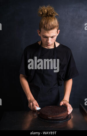 Männer Vorbereitung Schokolade Kuchen vor auf schwarze Wand Stockfoto