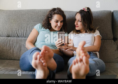 Mädchen in einer Couch mit Füßen in einer Tabelle Lachen mit Handy Stockfoto