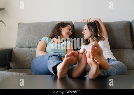 Zwei Mädchen lachend in eine Couch mit ihren Füßen auf einem Tisch Stockfoto