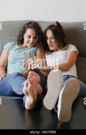 Mädchen in einer Couch mit Füßen in einer Tabelle auf der Suche nach einem Mobiltelefon Stockfoto