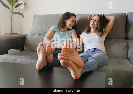 Zwei Mädchen in einer Couch mit ihren Füßen auf einem Tisch lachen Stockfoto