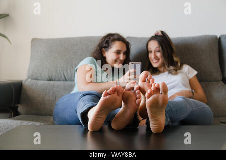 Mädchen in einer Couch mit Füßen in einer Tabelle mit einem Mobiltelefon Stockfoto