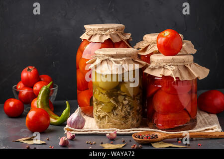 Verschiedene Arten von Dosentomaten, Hälften von Tomaten, grüne Tomaten mit Meerrettich im Glas für die langfristige Speicherung auf einem dunklen Hintergrund Stockfoto