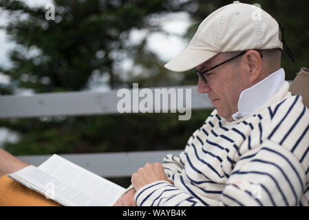 Mid-Adult Mann Lesebuch auf Deck Stockfoto