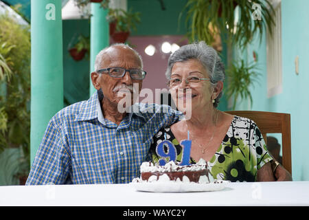 Ältere Paare mit einem Kuchen auf dem Tisch und die Nummer 91 auf dem Kuchen Stockfoto