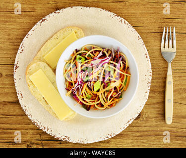 Thailändischer Nudelsalat mit Erdnusssoße und Scheiben von Cheddar Käse auf Zwiebel bun Schichten in overhead Komposition. Gesunde Ernährung Konzept. Stockfoto