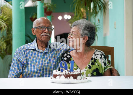 Ältere Paare mit einem Kuchen auf dem Tisch und die Nummer 91 auf dem Kuchen Stockfoto