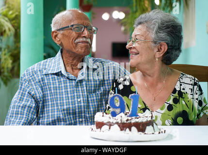 Ältere Paare mit einem Kuchen auf dem Tisch und die Nummer 91 auf dem Kuchen Stockfoto