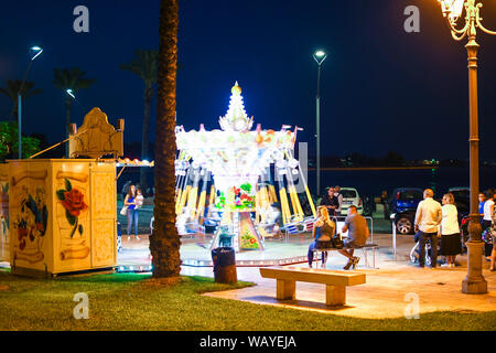 Ein kleines, buntes Karussell ist ein sich drehendes Blur als Eltern und lokalen Italiener genießen Sie den Abend auf der Piazza Vittorio Emanuele II in Brindisi Italien Stockfoto