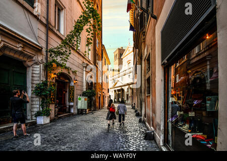 Touristen vorbei an Geschäften, einem schattigen Gasse in Richtung Saint Eustace Kirche mit dem Weißen Hirsch Skulptur auf dem Dach in Rom, Italien Stockfoto