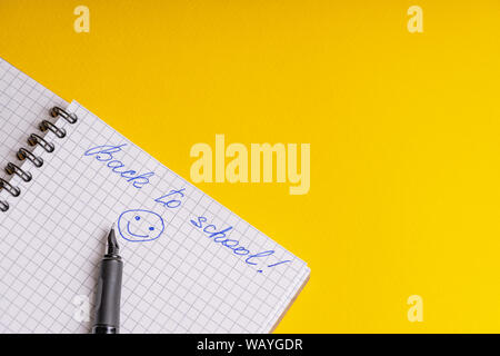 Die Inschrift zurück zu Schule und Lächeln auf eine quadratische Notizbuch und Kugelschreiber auf gelbem Hintergrund Stockfoto