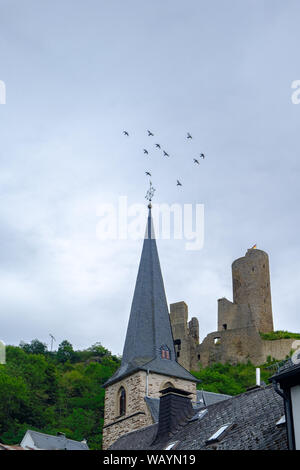 Pfarrkirche Kirche und Löwenburg schloss mit fliegenden Vögel im Hintergrund an der malerischen Ortschaft Monreal in der Eifel, Deutschland Stockfoto