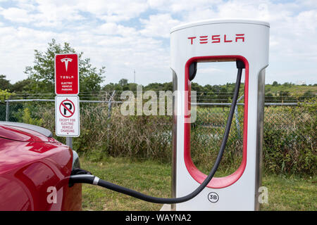 Tesla Kompressor Stall und Informationen zum Parken Schilder gesehen, während ein Tesla Model S angeschlossen ist und geladen wird. Stockfoto