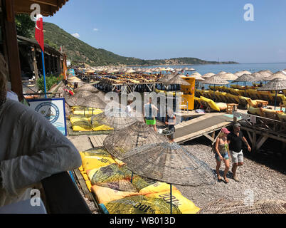 Direkt am Strand mit Liegestühlen und Sonnenschirmen auf Pfeilern über dem Wasser am Hafen von Assos an der Ägäischen Küste der Türkei. Stockfoto