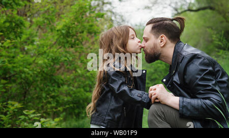 Modernes, stilvolles Familie Fuß in den Park. Tochter Küsse und Umarmungen Vati. Zeit zusammen. Familie suchen. Urban casual Outfit. Stockfoto