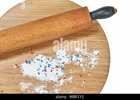 Eine hölzerne Rolling Pin auf einem Bambus Schneidebrett mit weißem Mehl und roten, weißen und blauen Streuseln auf dem Board isoliert auf weißem Stockfoto