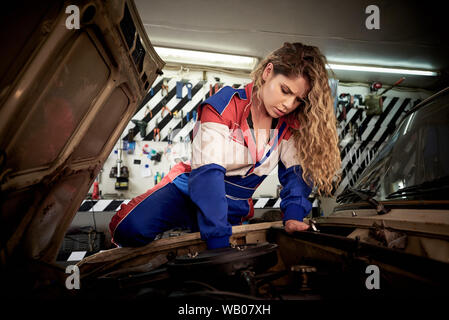 Eine junge Frau in Overalls auf eine Garage ist ein Auto zu reparieren. Stockfoto
