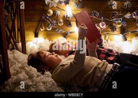 Kleine Mädchen und Jungen sind mit einem Buch in einem Zimmer für Weihnachten. Stockfoto