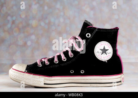 Rosa und schwarze Converse Sneaker gegen einen verschwommenen Hintergrund getragen hat Rosa Schnürsenkel Stockfoto