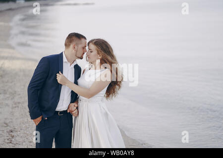 Schönen jungen langhaarigen Braut im weißen Kleid mit ihr junger Ehemann am Strand Stockfoto