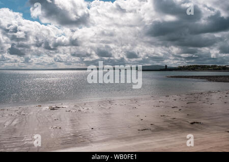 Sonne glitzert auf dem Sandstrand und ruhige See mit Blick auf Carrigaholt Castle im County Clare in Irland Stockfoto